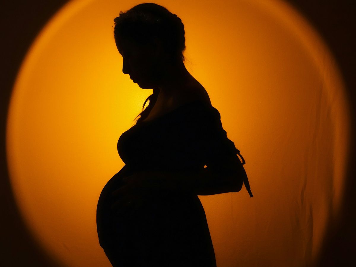 Mãos de uma gestante repousadas sobre a barriga, banhadas pela luz quente de uma janela ao fim de tarde.