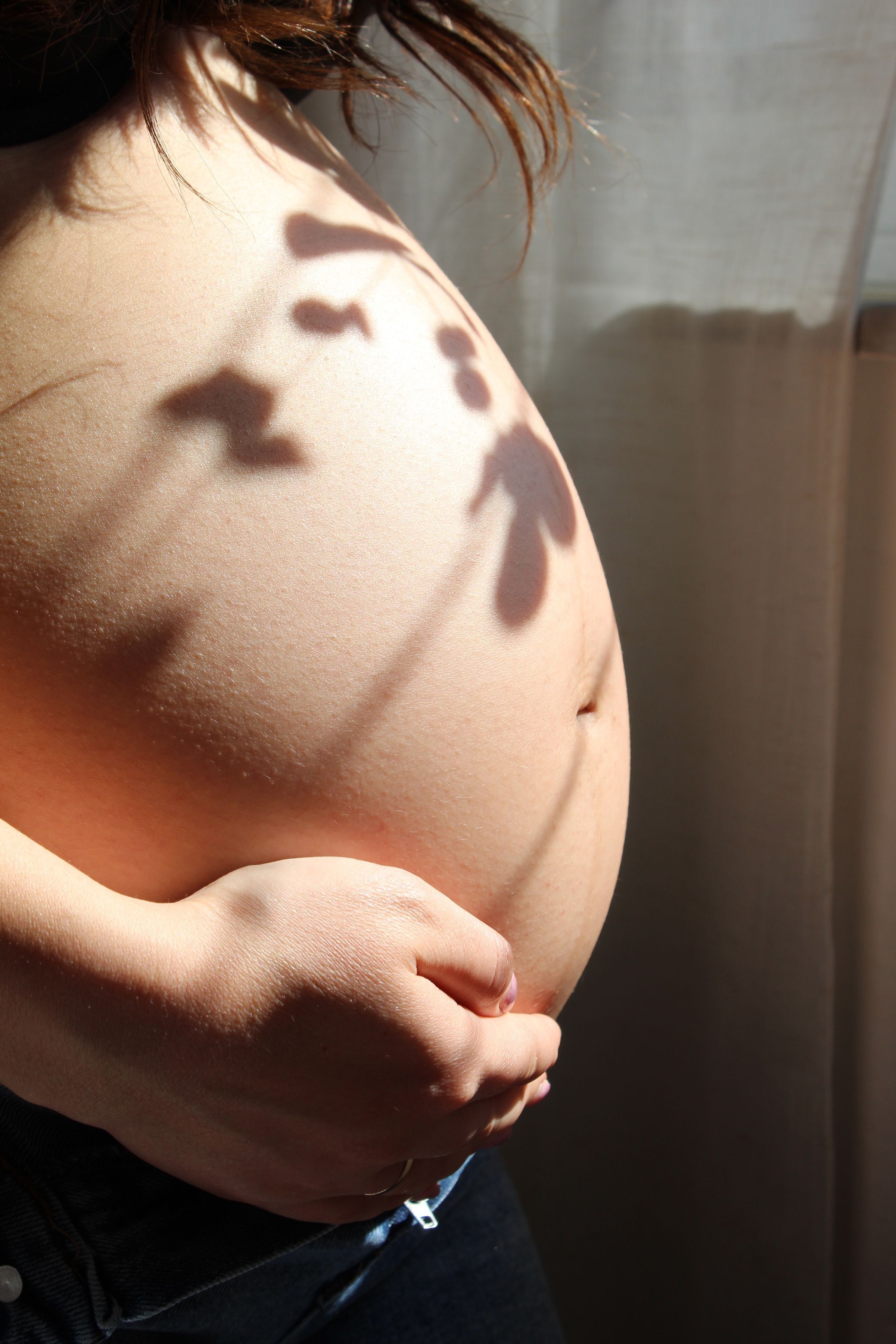 Mãos entrelaçadas repousando sobre uma barriga grávida em luz suave