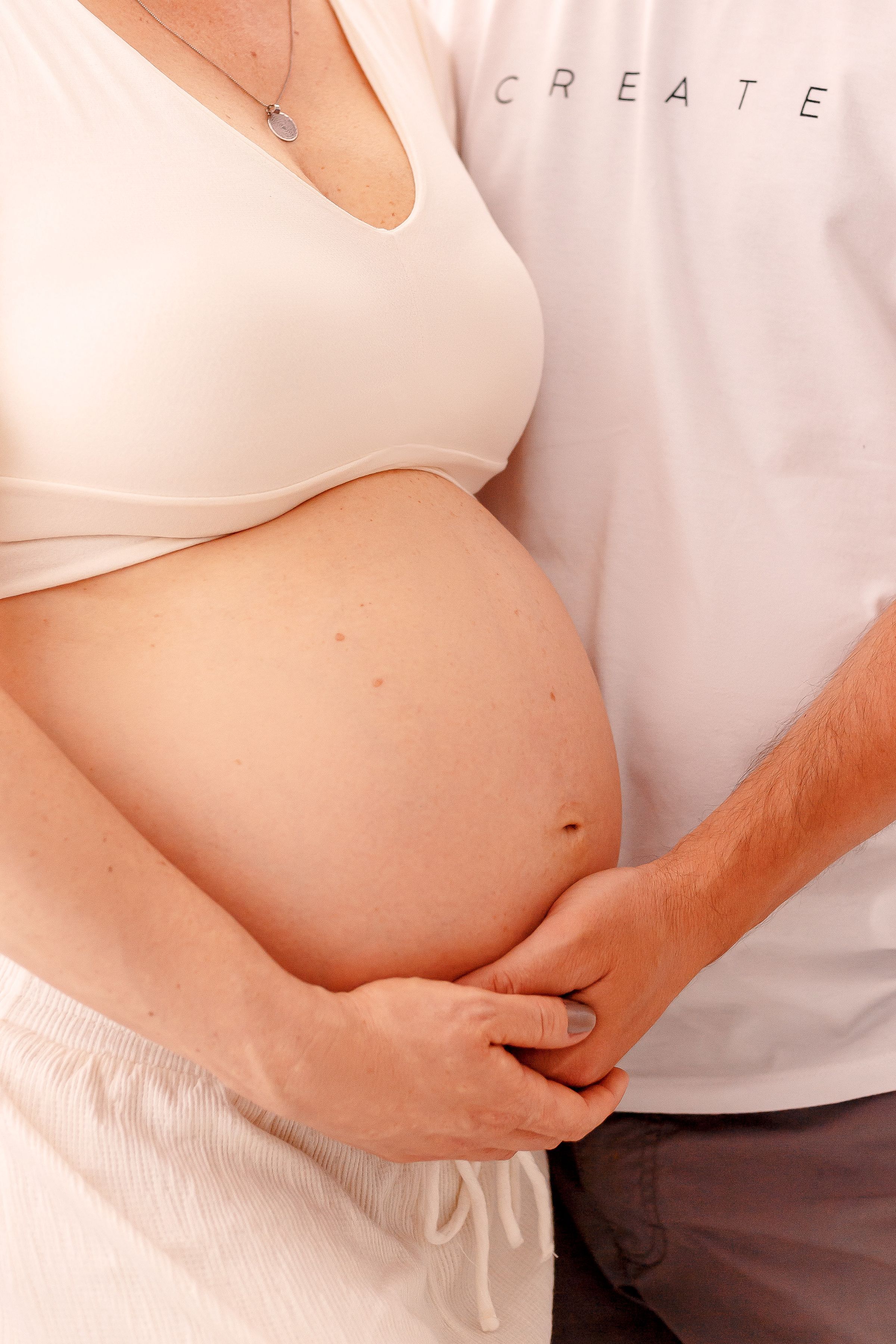 Mãos entrelaçadas repousando sobre uma barriga grávida em luz suave