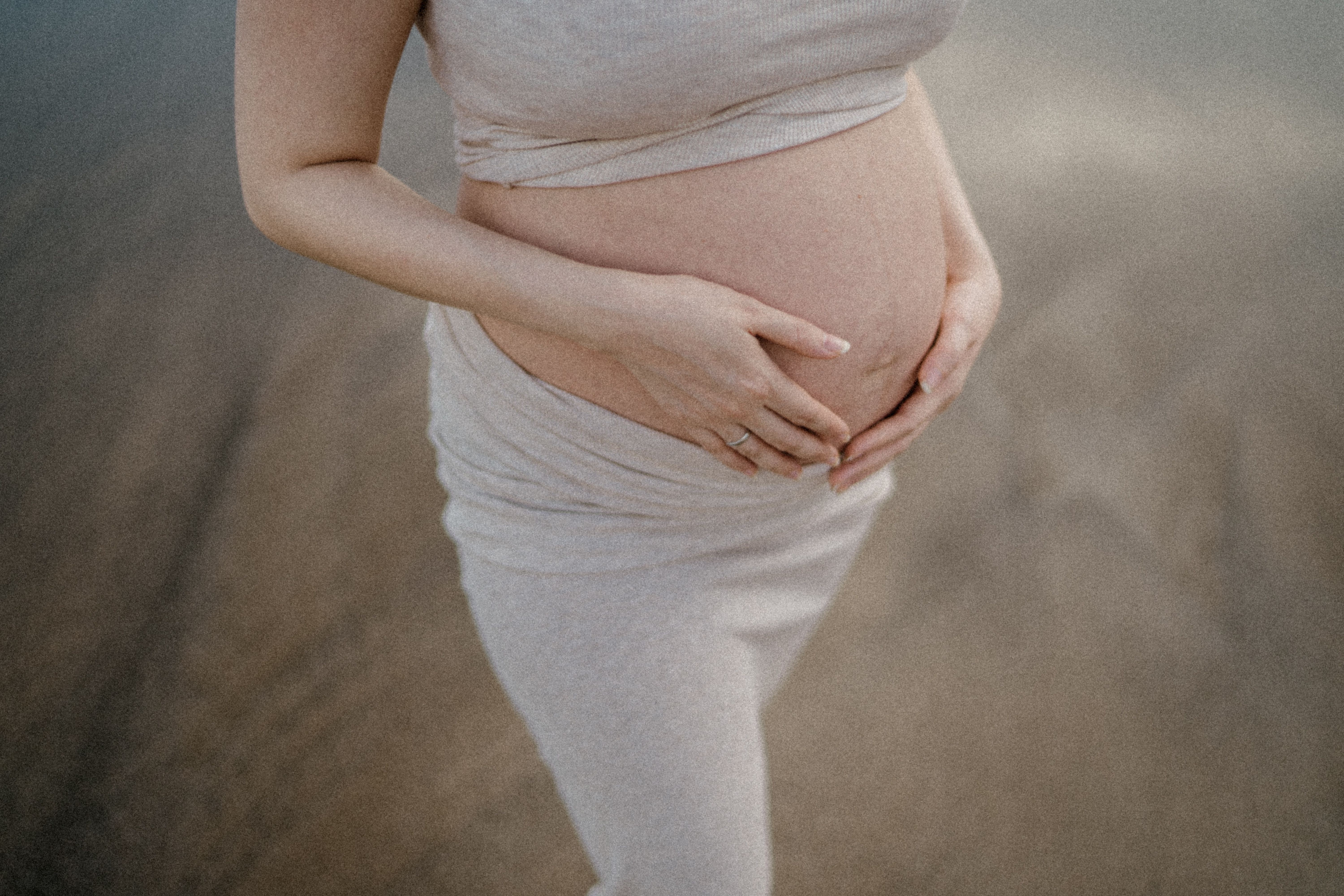 Mãos entrelaçadas repousando sobre uma barriga grávida em luz suave
