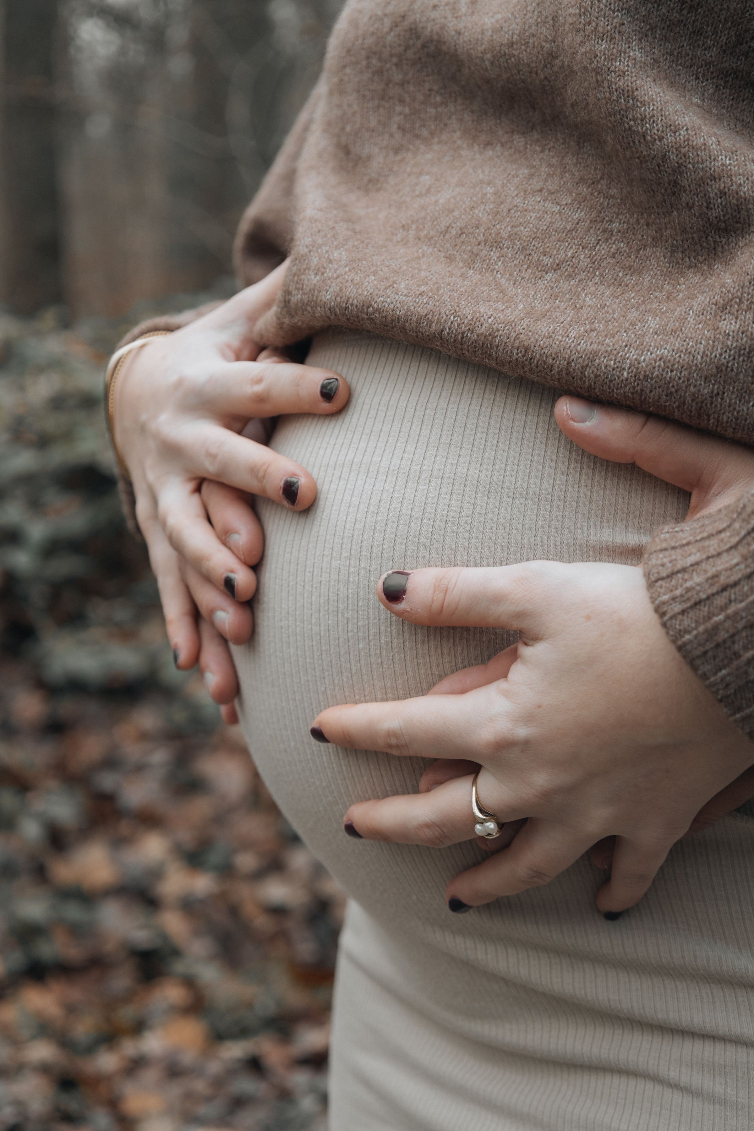 Mãos entrelaçadas repousando sobre uma barriga grávida em luz suave